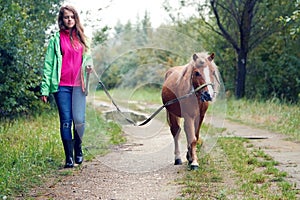 Teenage girl walking with a pony colt on a leash along a country dirt road