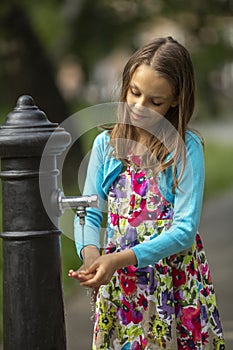 A teenage girl washes her hands in the park by the fountain.
