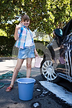 Teenage girl washing a car on a sunny day