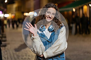 Teenage girl waving hands gesturing hi hello greeting or goodbye on urban city street at night
