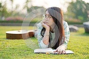 Teenage girl wearing glasses lying down with guitar and books On the field at sunset.