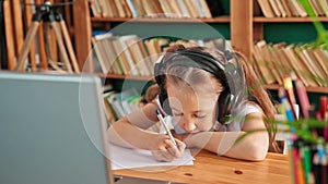 Teenage girl wearing headphones studying online from home with distance teacher. Teen school student distance learning