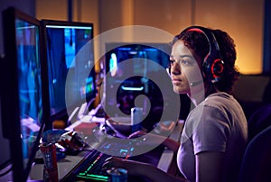 Teenage Girl Wearing Headset Gaming At Home Using Dual Computer Screens