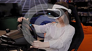 A teenage girl wearing virtual reality glasses sits in a car driving simulator.