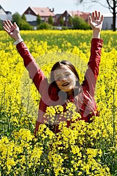 Teenage girl welcomes spring in a field with yellow rapeseed flowers