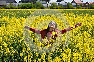 Teenage girl welcomes spring in a field with yellow rapeseed flowers