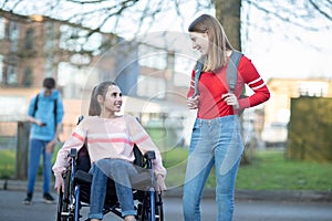 Teenage Girl In Wheelchair Talking With Friend As They Leave High School