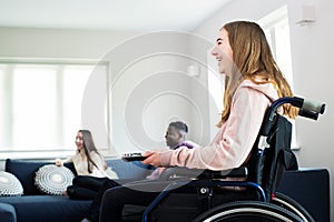 Teenage Girl In Wheelchair Watching Television With Freinds At Home