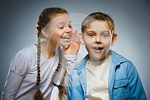 Teenage girl whispering in ear of boy on gray background. Communication concept