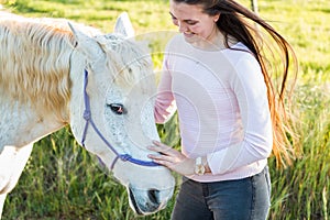 Teenage girl with a white Boerperd horse standing by his head petting his nose