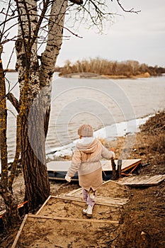 Teenage girl in winter clothes going down the stairs on the ice on the bank.