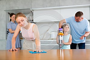 Teenage girl wiping kitchen table while cleaning apartment with family