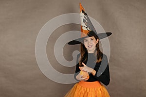 Teenage girl in witch costume for Halloween on gray background holding small pumpkins in her hands, copy space