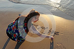 A teenage girl writes on the sand in the beach