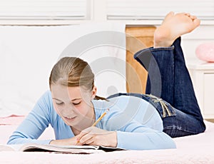 Teenage girl writing in notebook on bed