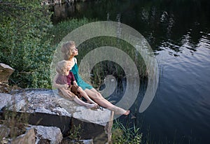 teenage girl and a boy, brother and sister, are happily sitting together on rock near lake and fantasize with interes photo