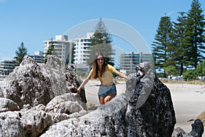 Teenage girl in yellow top and denim short pants climbs rocks