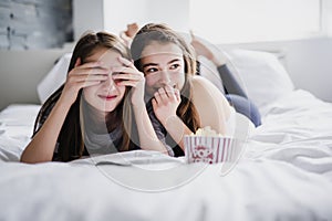 Teenage girls eating popcorn and watching horror movie on tv at home