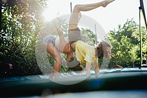 Teenage girls friends outdoors in garden, doing exercise on trampoline, having fun, jumping.