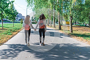 Teenage girls in sweaters, back view, walk with backpacks behind, summer in autumn and spring in the city, weekend after