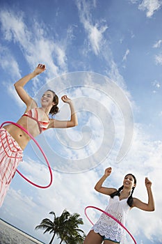 Teenage Girls Twirling Hula Hoops On Beach