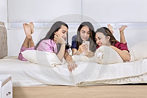 Teenage girls using a cellphone and confide on bed