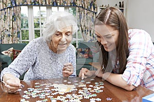 Teenage Granddaughter Helping Grandmother With Jigsaw Puzzle