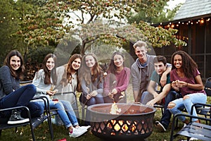 Teenage group sitting around a fire pit smiling to camera