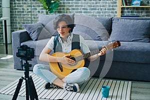 Teenage guitarist recording video for internet blog holding guitar at home