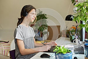 Teenage guy in headphones sitting at home using computer and a graphics tablet