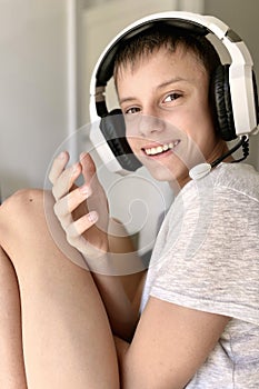 A teenage guy smiles sincerely while sitting at a computer in white headphones