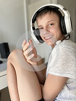 A teenage guy smiles sincerely while sitting at a computer in white headphones photo