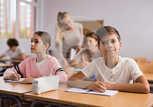 Teenage high school students studying in college with classmates, making notes of teacher lecture