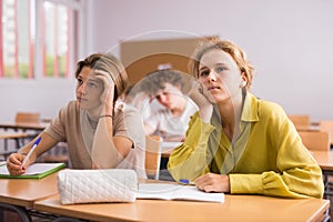 Teenage high school students studying in college with classmates, making notes of teacher lecture