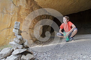 Teenage kid looking at mountain view from rock cave with stone cairn at foreground