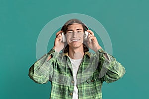 Teenage leisure. Happy millennial guy listening to music in headset on color background