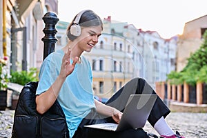 Teenage male student in headphones using laptop making video call