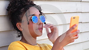 Teenage mixed race African American girl young woman wearing sunglasses reflecting blue sky and clouds using cell phone