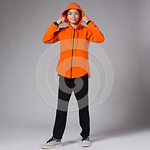 Teenage model in an orange hoodie and black trousers, a hood thrown over her head, studio shot
