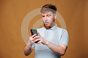 A teenage redhead guy in a studio shot, shocked and staring at his smartphone