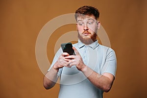 A teenage redhead guy in a studio shot, shocked and staring at his smartphone