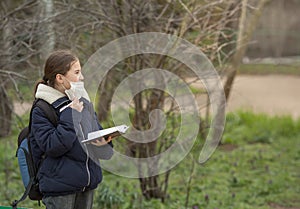 A teenage schoolgirl girl is sitting on a bench  and writes with a pen in a notebook