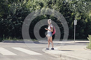 Teenage schoolgirl with headphones and mobile phone on pedestrian crossing