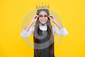 Teenage selfish girl celebrates success victory. Teen child in queen crown isolated on yellow background. Princess in