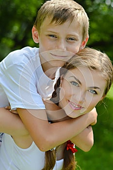 Teenage sister and little brother happy smiling & looking at camera embracing outdoors