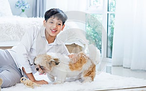 Teenage smart boy wearing casual shirt, smiling with happiness, playing together with little dog or pet with fun, relaxation, love