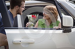Teenage son handing his mom a red rose in the car.