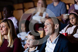 Teenage son watches movie with his parents and eats popcorn in cinema hall