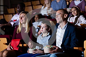 Teenage son watches movie with his parents and eats popcorn in cinema hall