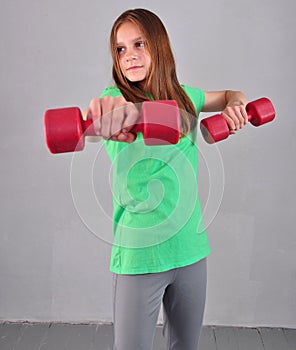 Teenage sportive girl is doing exercises with dumbbells to develop muscles on grey background. Sport healthy lifestyle concept. Sp